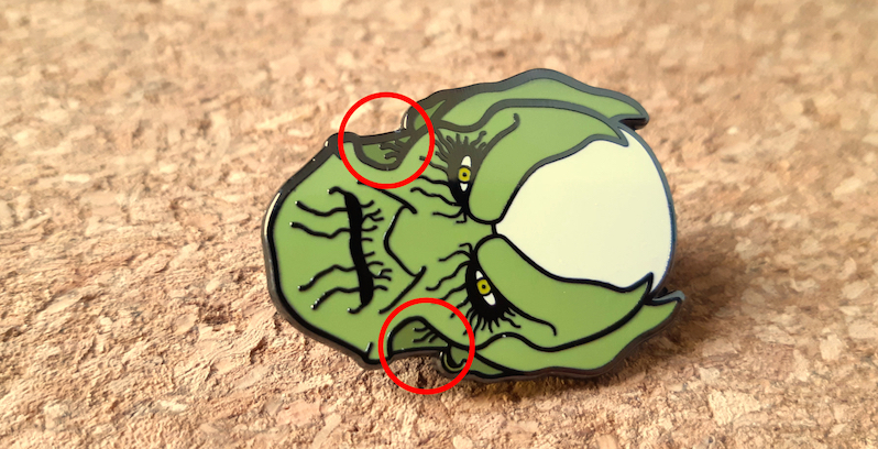 An enamel pin of a face with inconsistent sizing on the played lines